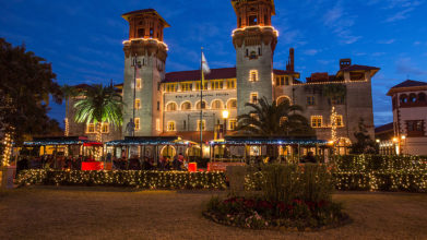 St. Augustine old town trolley driving past lightner museum at night decorated with holiday lights