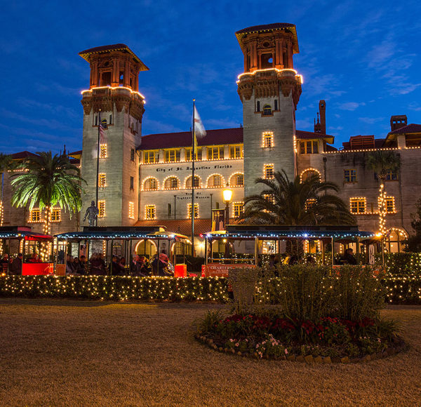 St. Augustine old town trolley driving past lightner museum at night decorated with holiday lights