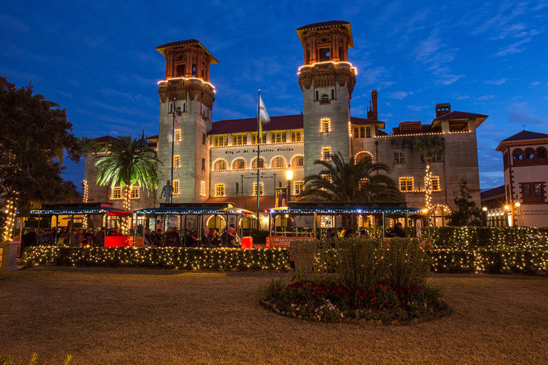 St. Augustine old town trolley driving past lightner museum at night decorated with holiday lights