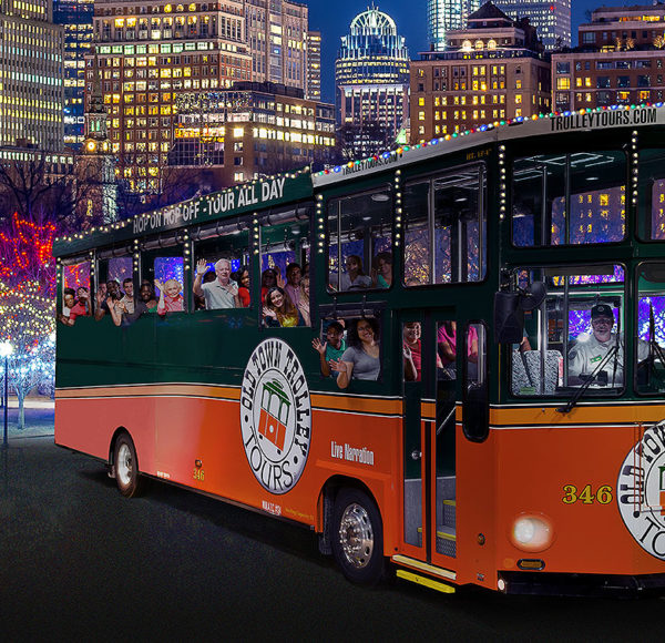 night time picture of trolley in front of Boston skyline and holiday lights