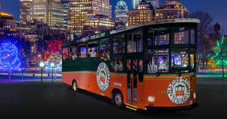 night time picture of trolley in front of Boston skyline and holiday lights