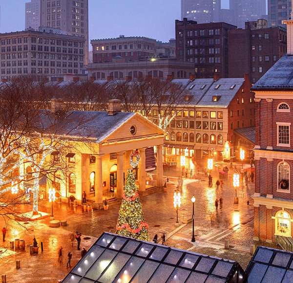 Nighttime picture of Faneuil Hall in Boston during Christmas with various trees decorated in holiday lights