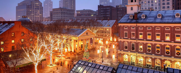 Nighttime picture of Faneuil Hall in Boston during Christmas with various trees decorated in holiday lights