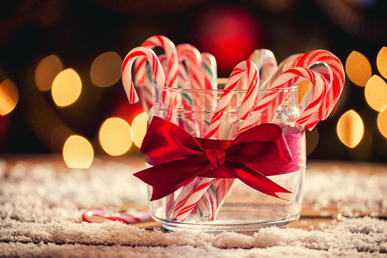 glass container wrapped in a ribbon and holding candy canes; in the background are holiday lights