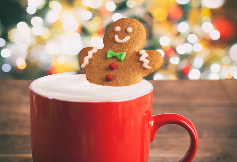a red mug with hot cocoa and a gingerbread man cookie; and in the background are holiday lights