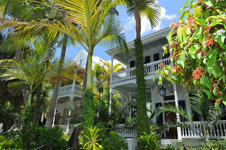 Key West two-floor houses with wrap-around porches and surrounded by foliage including palm trees