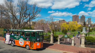 Boston trolley driving past Boston Public Garden and city skyline in the background
