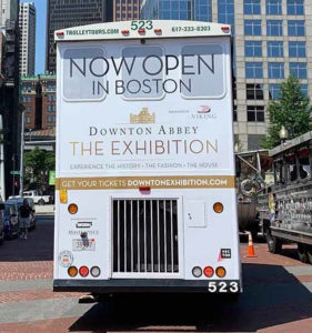 boston trolley showing an advertisement covering the entire back with the words 'Now Open In Boston Downtown Abbey Exhibition'