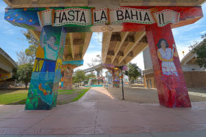 picture of barrio logan mural artwork painted on pilons underneath highways with the words 'HASTA LA BAHIA !!'