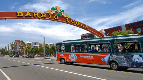 san diego trolley driving through neighborhood and past an arch that reads 'barrio logan'