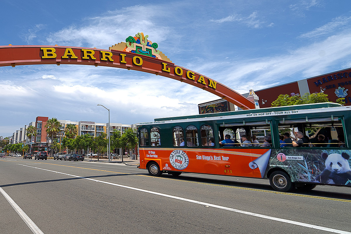 san diego trolley driving through neighborhood and past an arch that reads 'barrio logan'