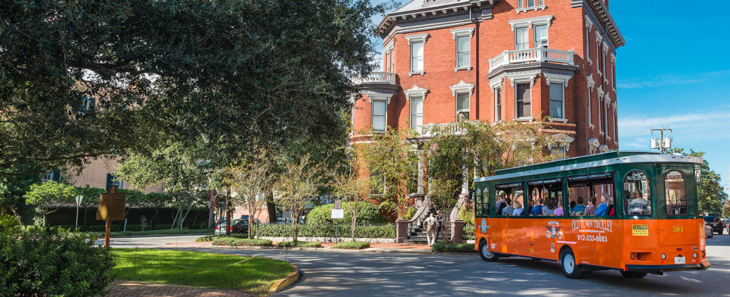 savannah trolley driving past kehoe house made of bricks with many trees on the left