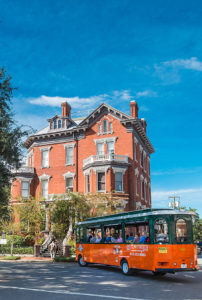 savannah trolley driving past kehoe house made of bricks with many trees on the left