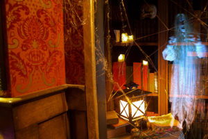 indoor picture of a spooky looking room with a library, table, lantern, spider webs and a ghost