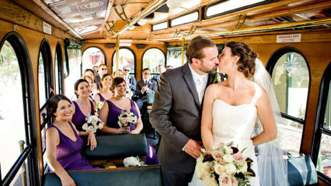 wedding couple kissing inside trolley while wedding party sits in the background