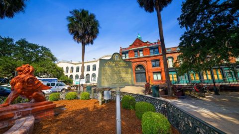 A placard that reads 'old Savannah Cotton Exchange' next to a statue of a gryphon with the cotton exchange building in the background