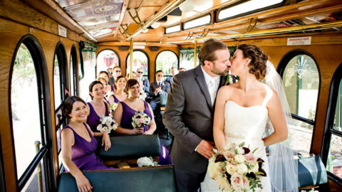 interior of a trolley featuring a bride and groom standing and kissing and the wedding party seated and watching them in the background